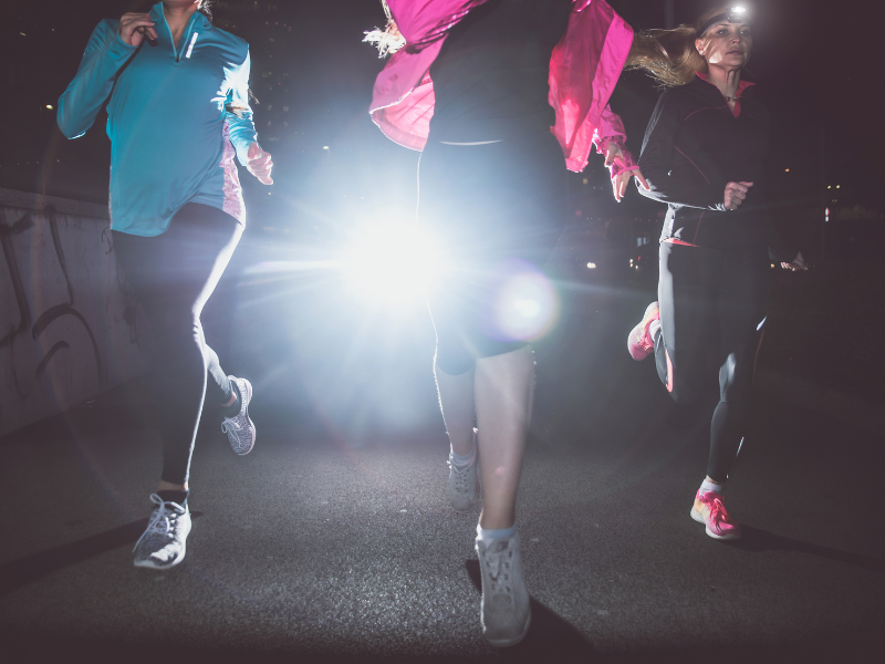 3 female runners on the road using headtorches for safety